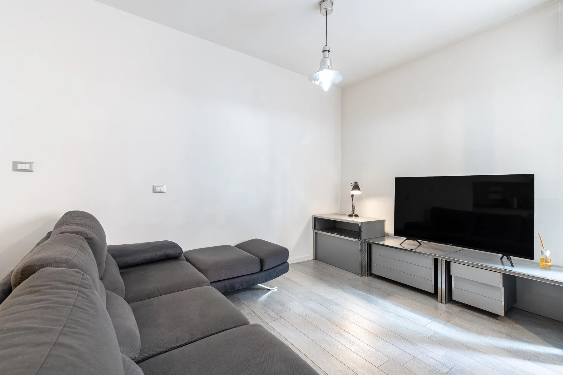 Sala de estar con asientos grises y un televisor sobre un mueble bajo.