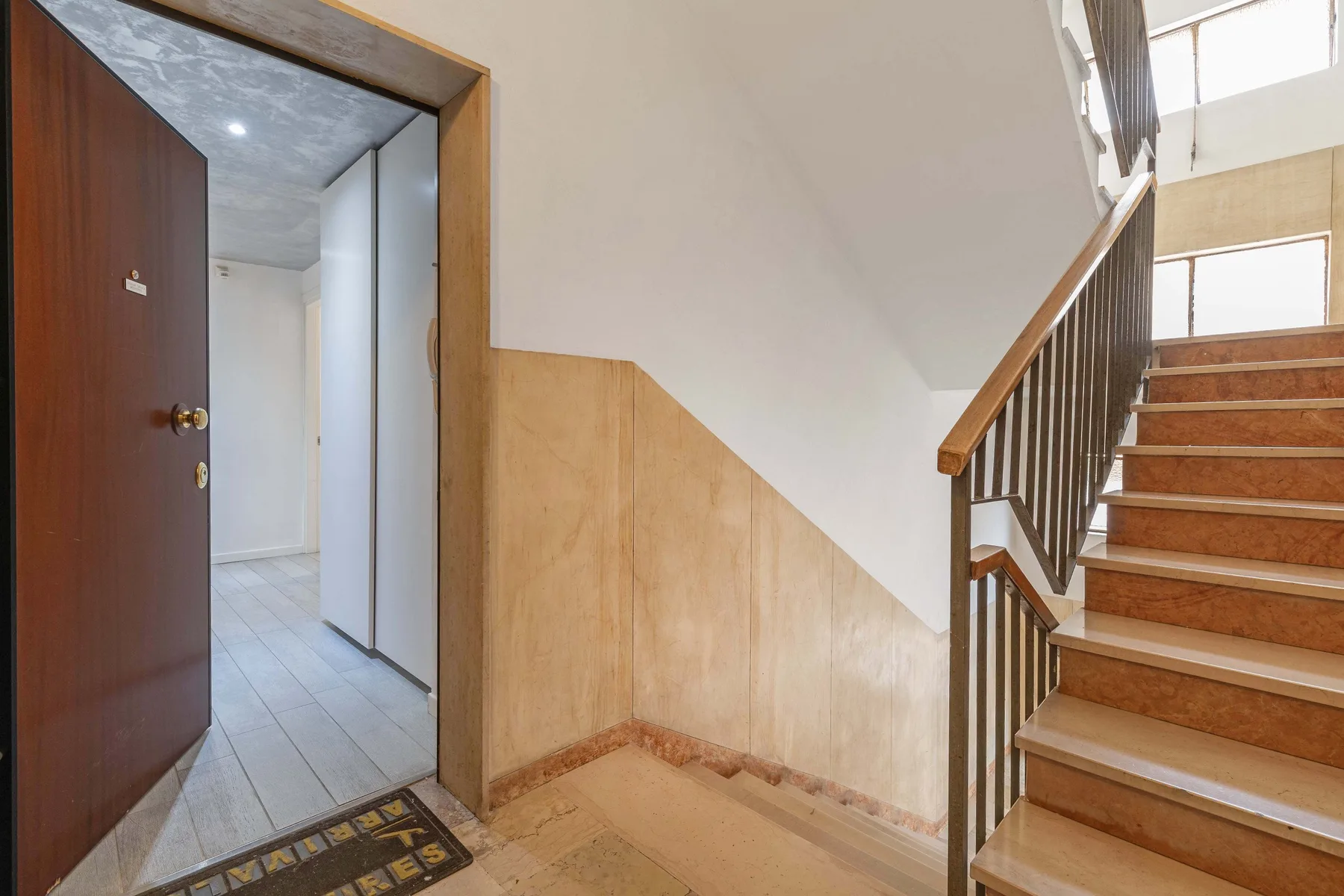 Una entrada interior queda junto a una escalera de peldaños de madera y barandilla.