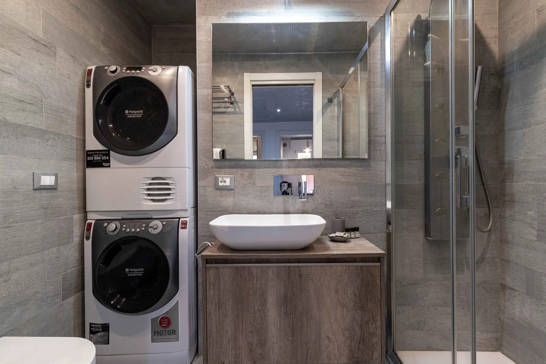 Un baño moderno con lavabo, espejo, ducha y lavadoras apiladas.