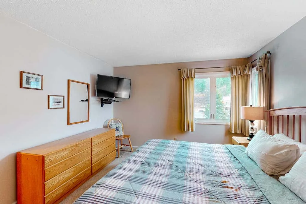 A bedroom with a bed, wooden dresser, and window with curtains.