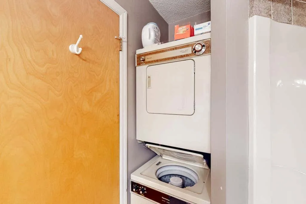 A laundry area with a stacked washer and dryer beside a wooden door.