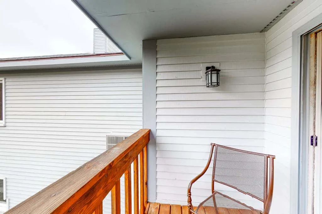 A small outdoor porch with a wooden railing and metal seating.