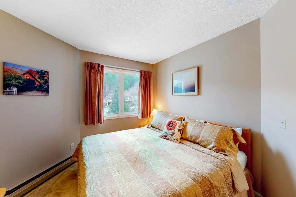 A bedroom with a bed beneath a window framed by rust-colored curtains.