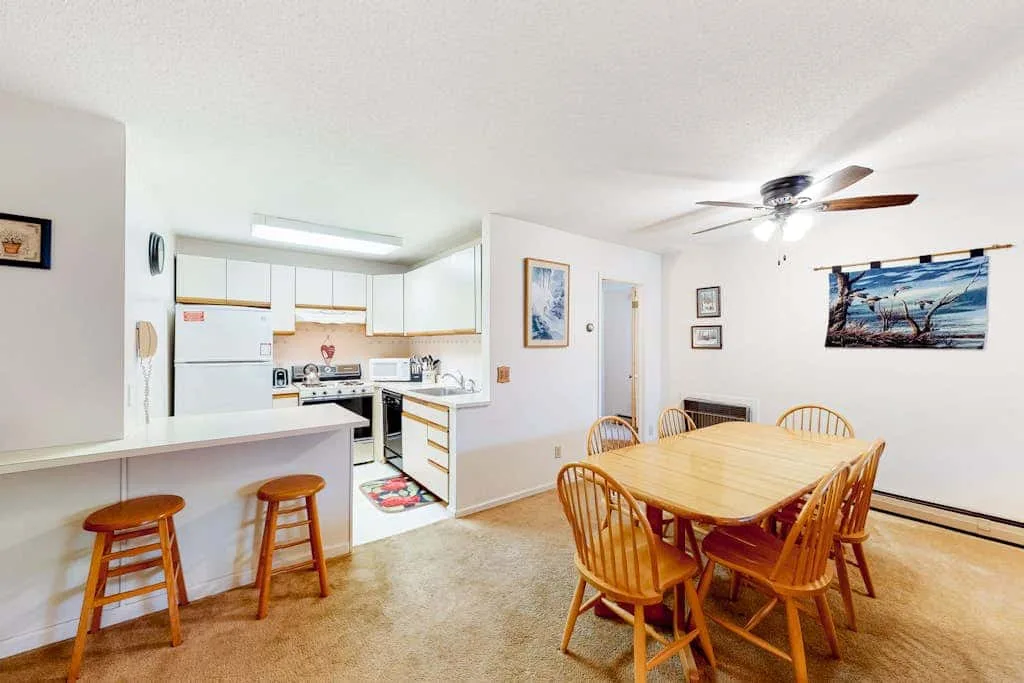An open dining area with a wooden table and a kitchen in the background.