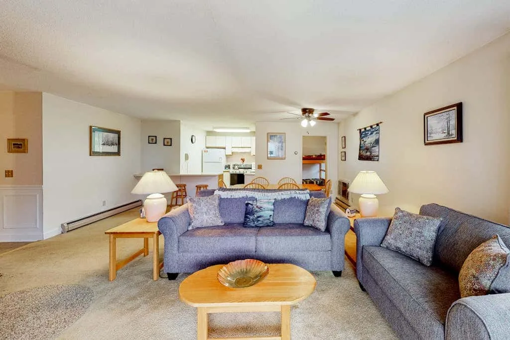 A living room with seating and a coffee table, opening onto a kitchen.