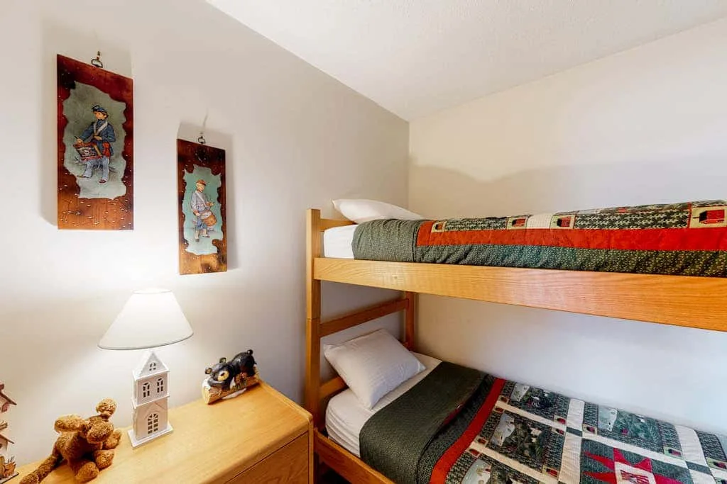 A bunk bed with patterned bedding sits beside a small wooden bedside table.