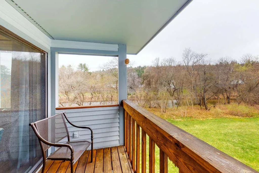 A covered wooden balcony overlooks a grassy yard and leafless trees.