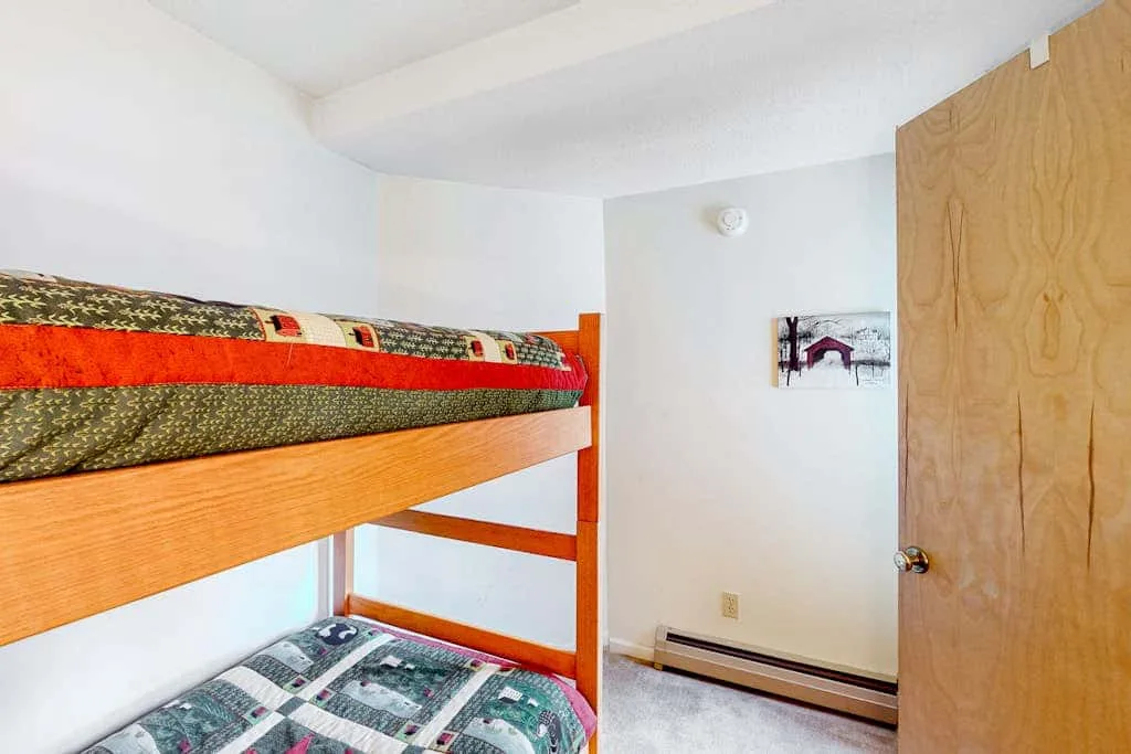 A bedroom with a wooden bunk bed and patterned bedding.