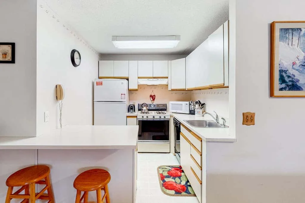 A compact kitchen with white cabinets, a stove, and a breakfast counter.