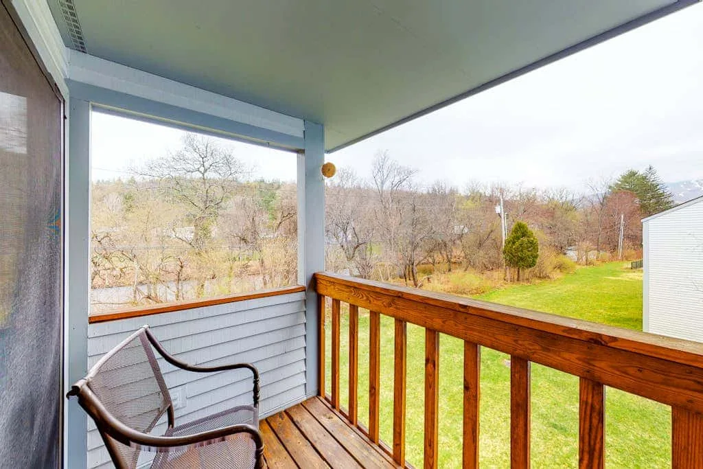 A covered porch with a wooden railing overlooks a grassy yard.