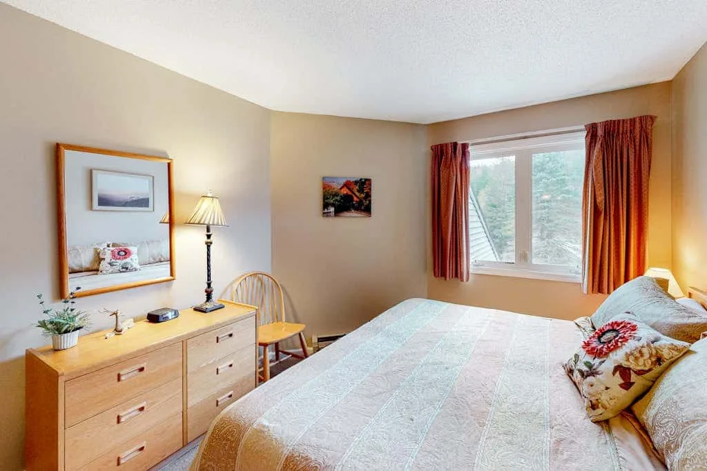 A bedroom with a bed, dresser, and a window framed by red curtains.