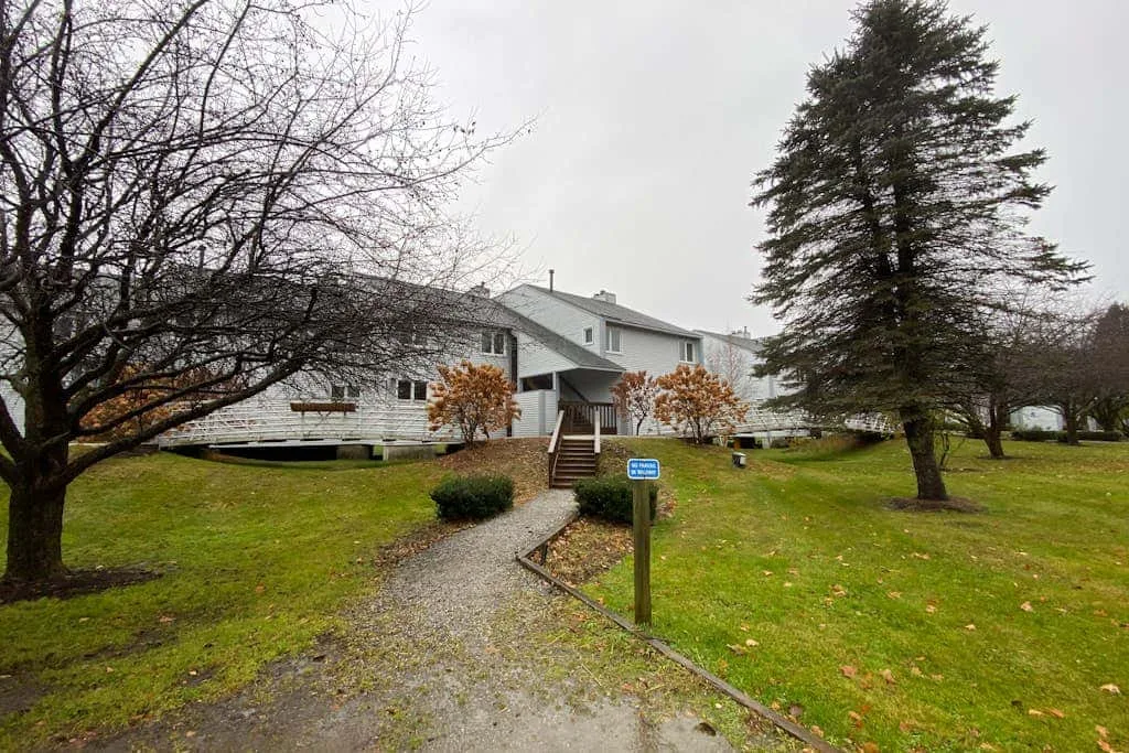 A light-colored house stands beside a gravel path on a grassy lawn.
