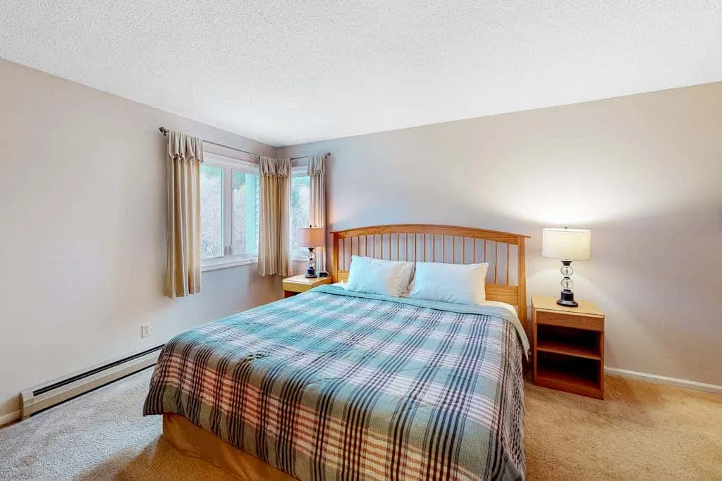 A bedroom with a wooden bed, plaid bedding, and windows with curtains.