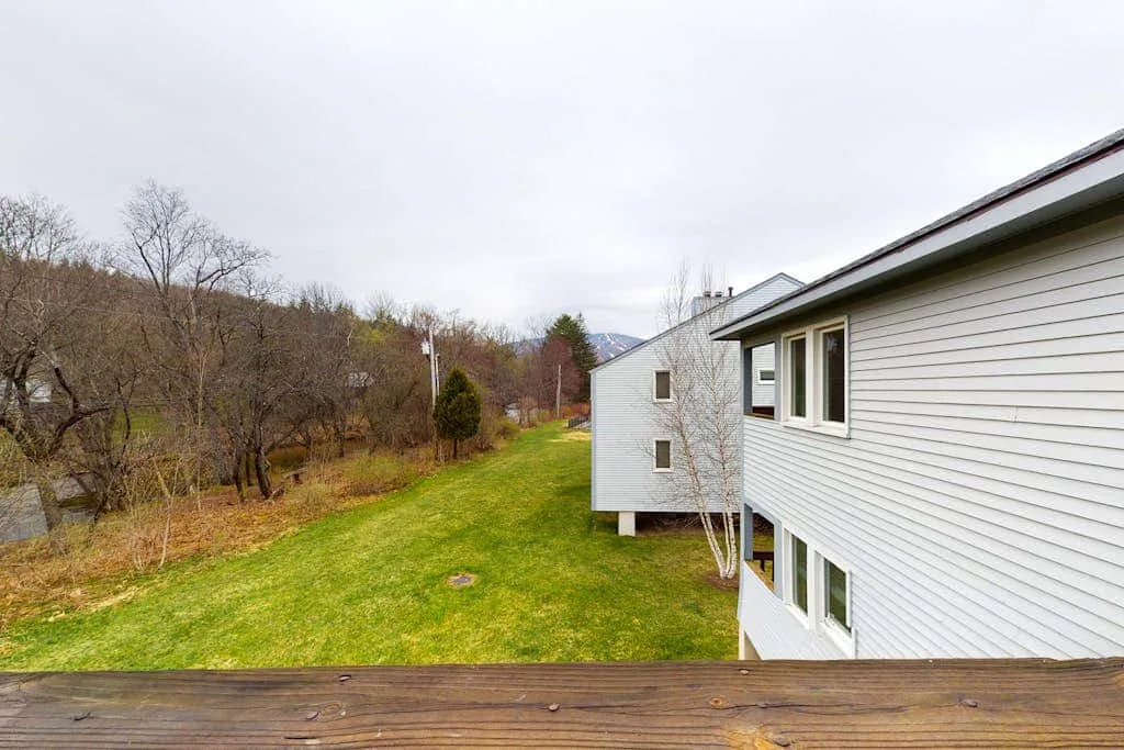 A grassy yard beside a white-sided building, viewed from a wooden deck.
