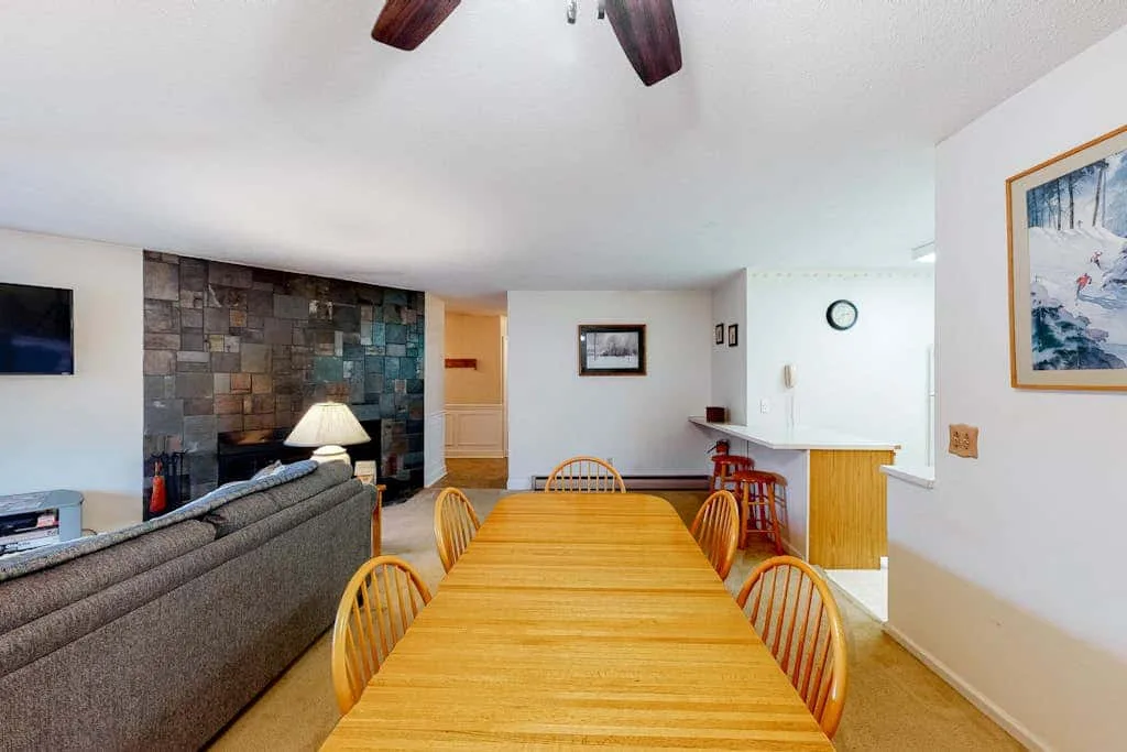 A dining area with a wooden table beside a living room and stone accent wall.