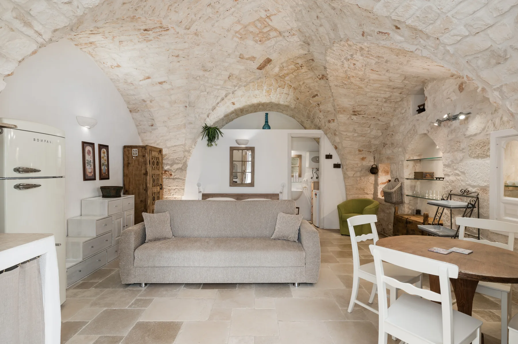 A vaulted stone living and dining room with a sofa and a wooden table.