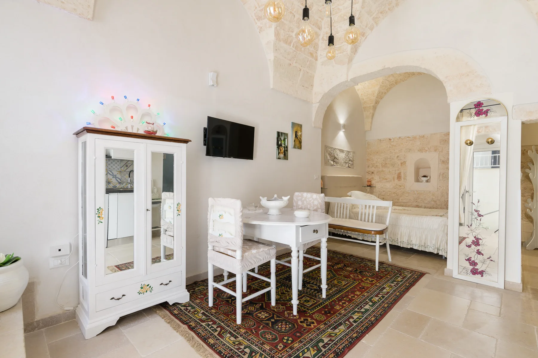 A bedroom and dining area share a bright room with arched stone details.