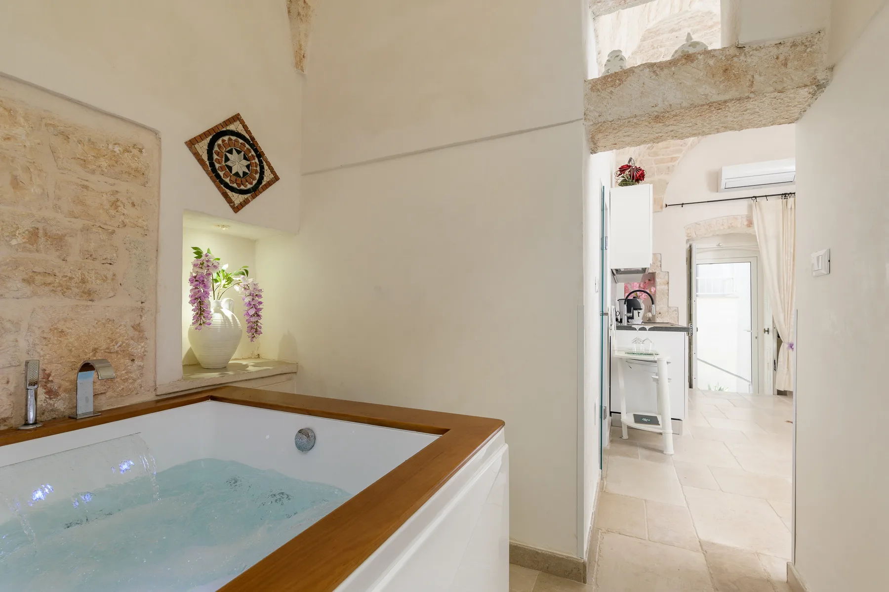 A bathroom with a built-in soaking tub, opening onto a bright adjoining room.