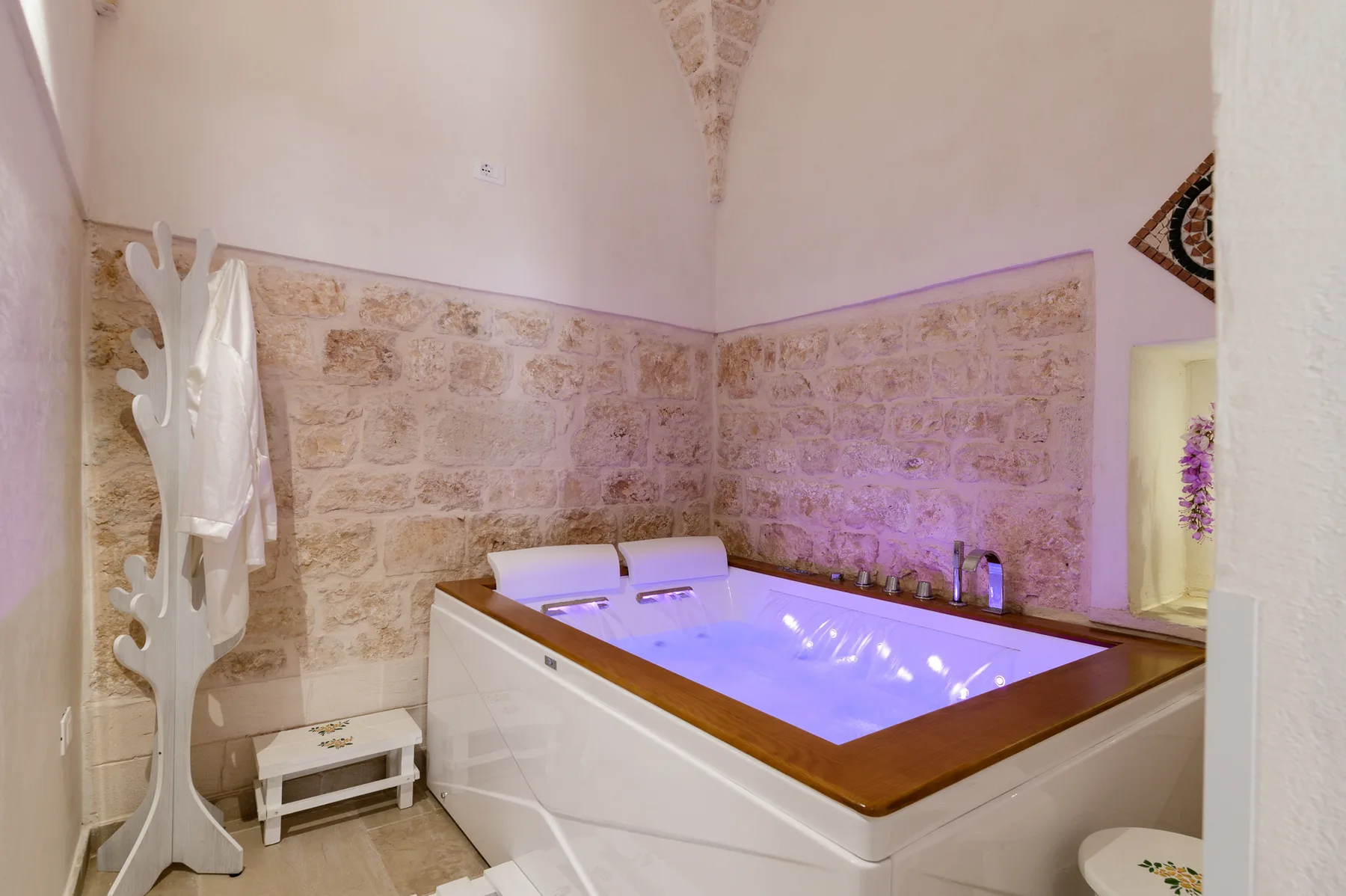 A bathroom with a large built-in bathtub and stone-patterned wall tiles.