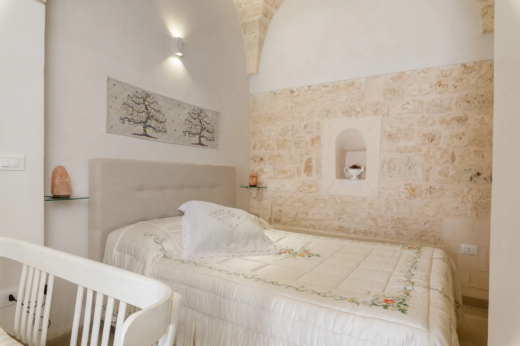 A bedroom with a bed, pale stone walls, and a small wall niche.