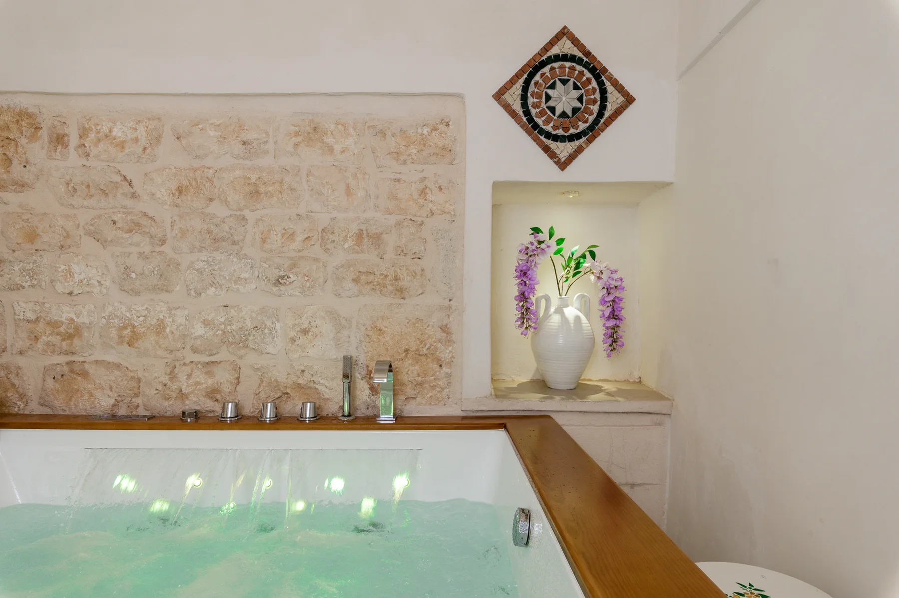 A tiled indoor pool beside a stone wall and a decorative vase.