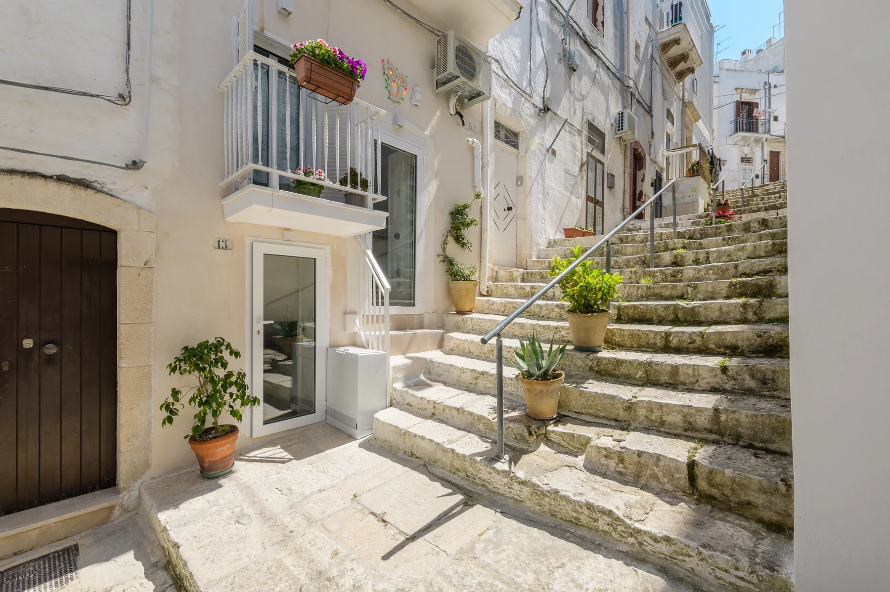 A stone stairway rises beside white buildings, with potted plants along the steps.