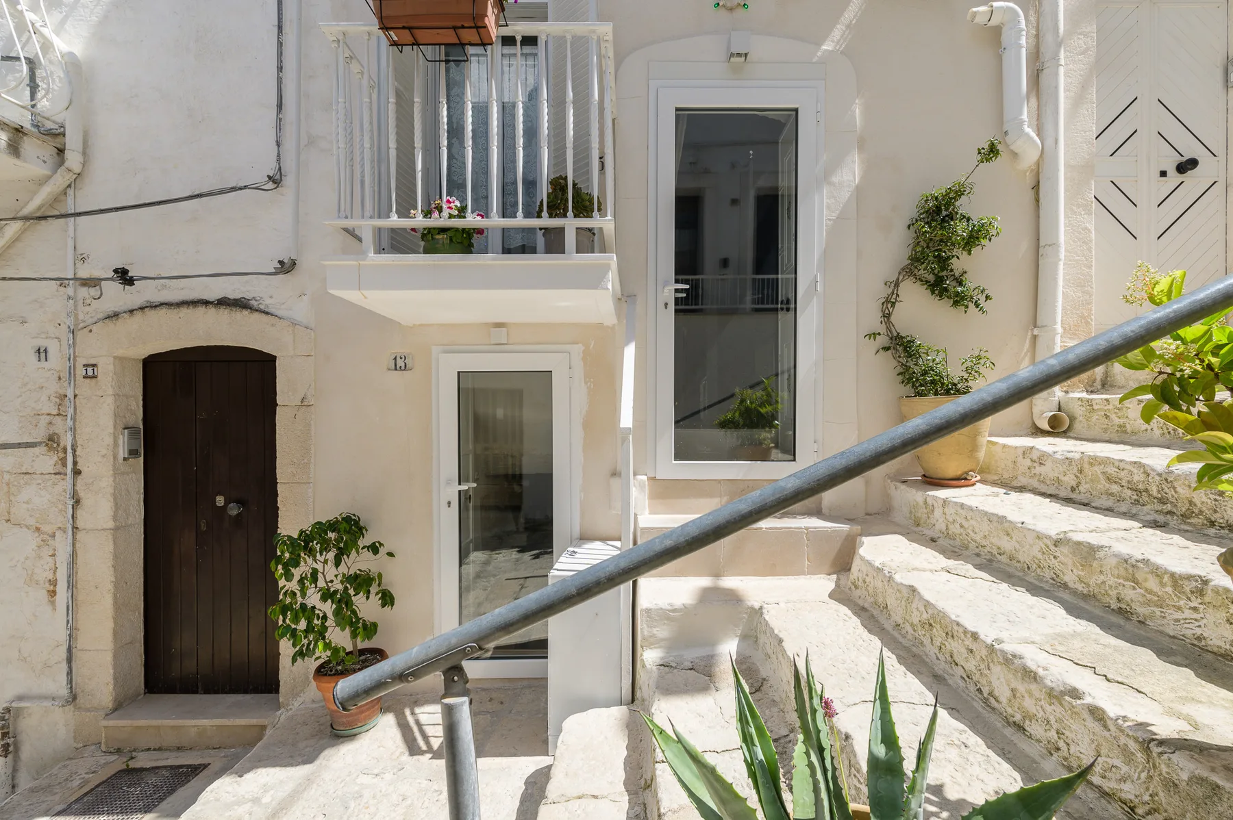 A white building entrance with dark doors, a balcony, and outdoor steps.