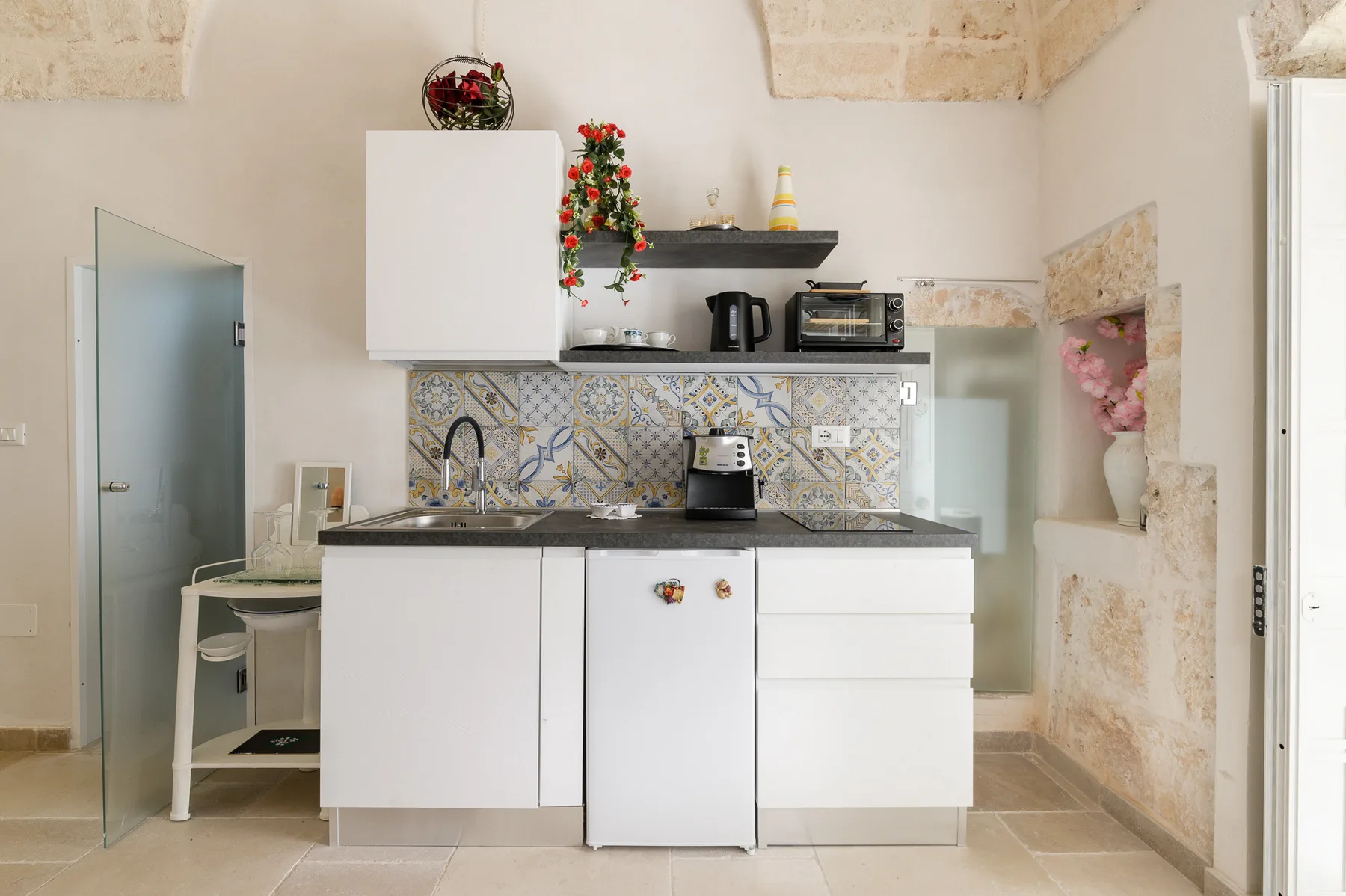 A compact kitchen with white cabinets, a dark countertop, and patterned tile backsplash.