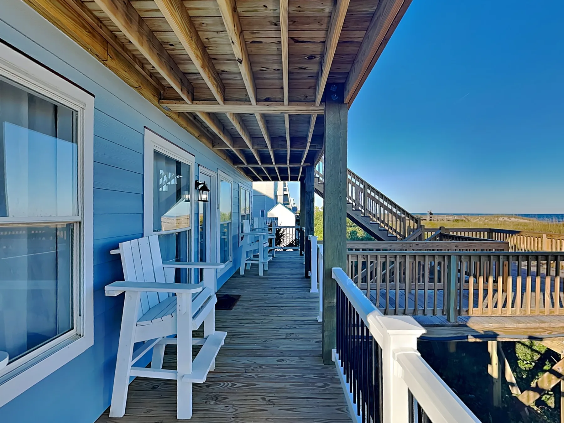A covered wooden porch with blue walls, seating, and a railing.