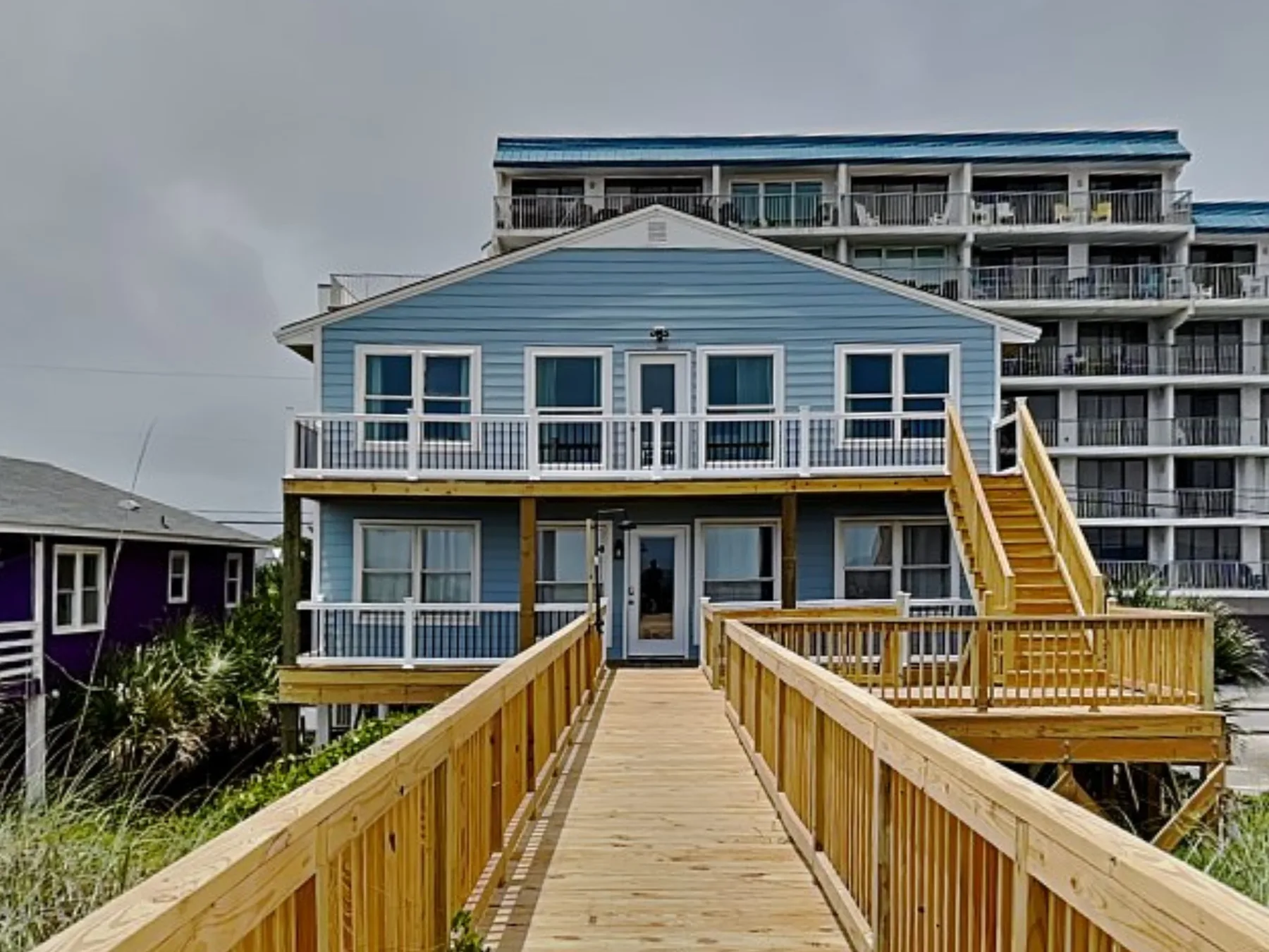 A blue coastal-style building stands at the end of a wooden walkway.