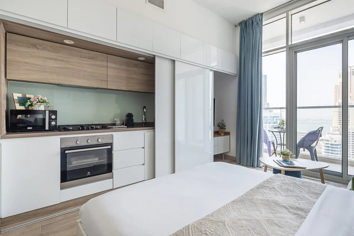 Un estudio luminoso con una cocina compacta y una gran ventana junto a la cama.