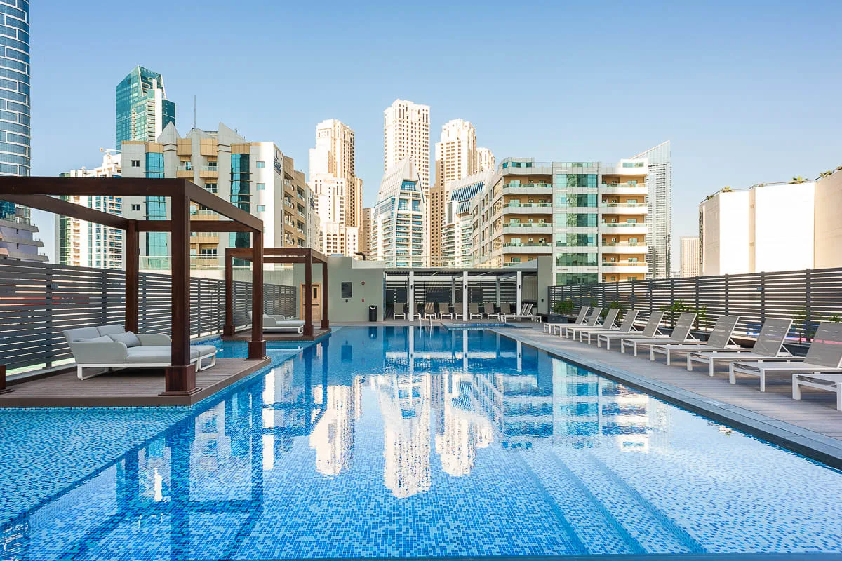 Una piscina en la azotea con tumbonas y edificios de la ciudad al fondo.