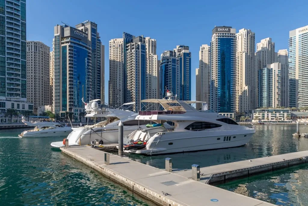 Un gran yate está amarrado en un puerto deportivo, con edificios altos detrás.