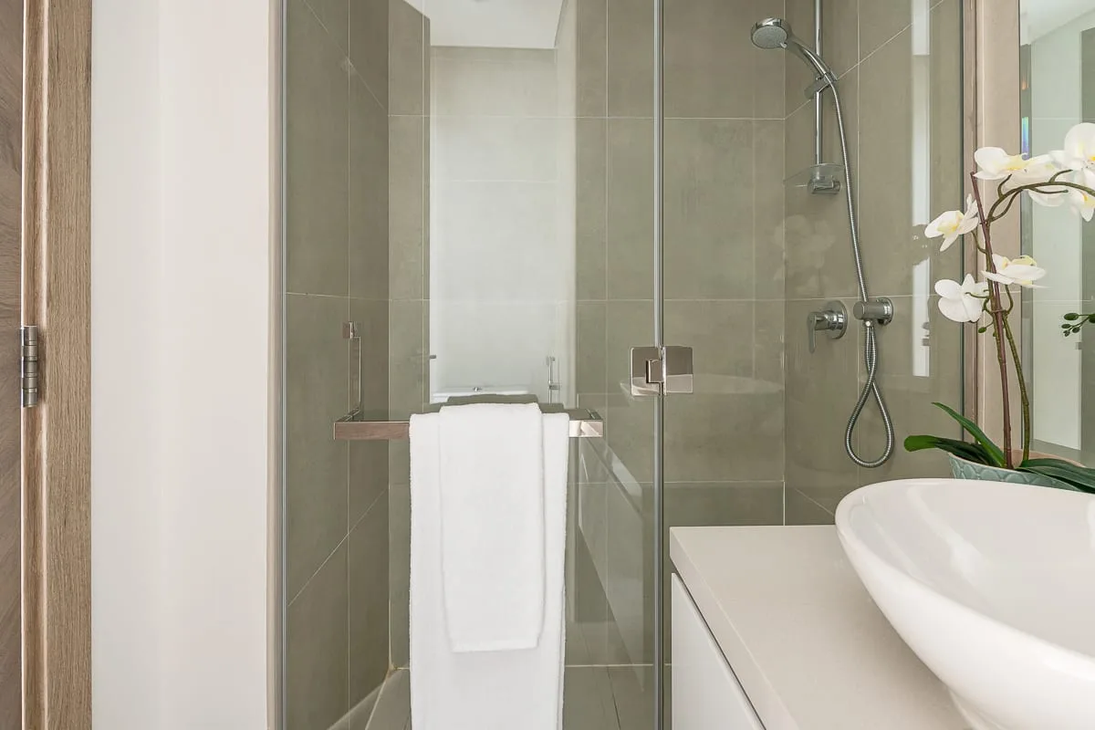 Un baño moderno con ducha de vidrio, lavabo blanco y una orquídea.