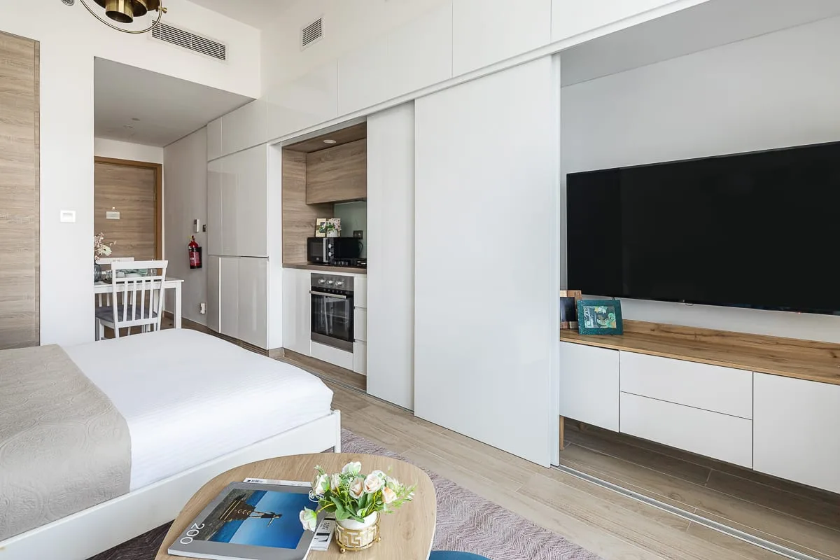 Un dormitorio moderno con cama, televisor y una pequeña cocina.