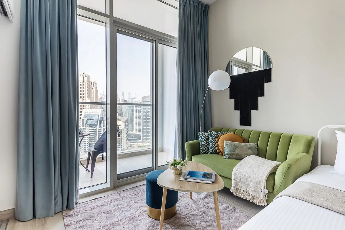 Una sala luminosa con asientos verdes y ventanales de piso a techo.