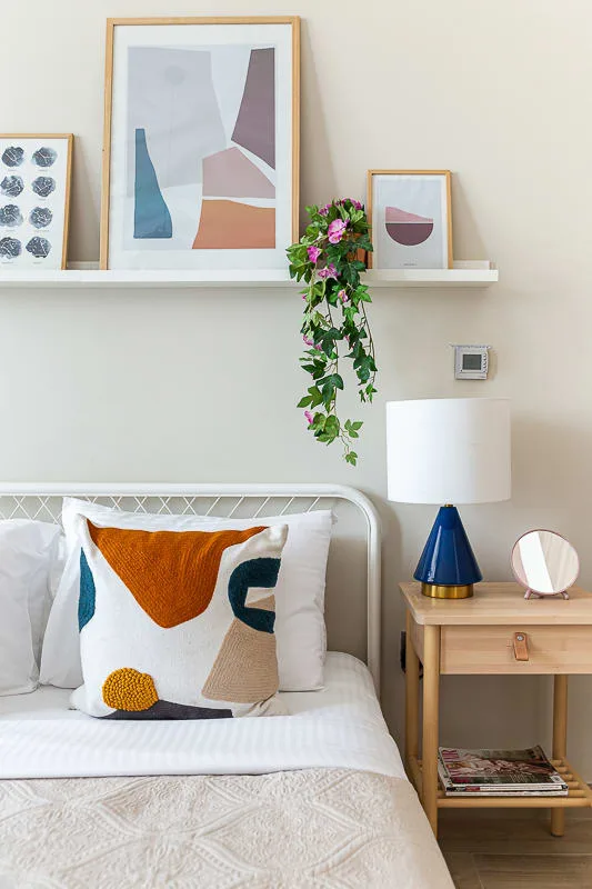 Un dormitorio con una cama blanca, cojines coloridos y cuadros sobre el cabecero.