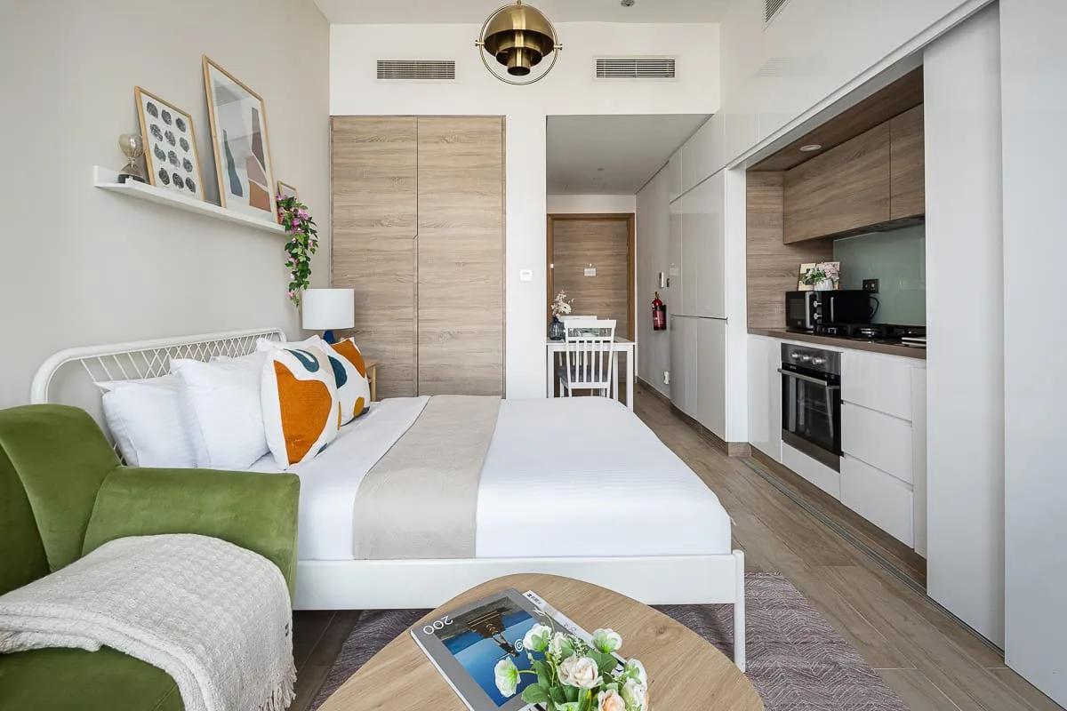 Un dormitorio compacto con una cama tendida y una pequeña cocina junto a la pared.