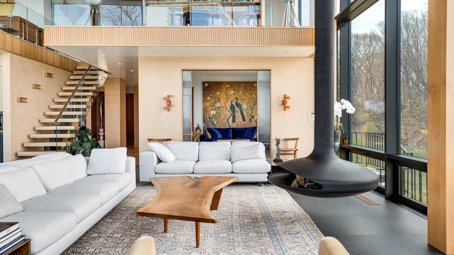 A bright living room with seating, a sculptural fireplace, and large windows.