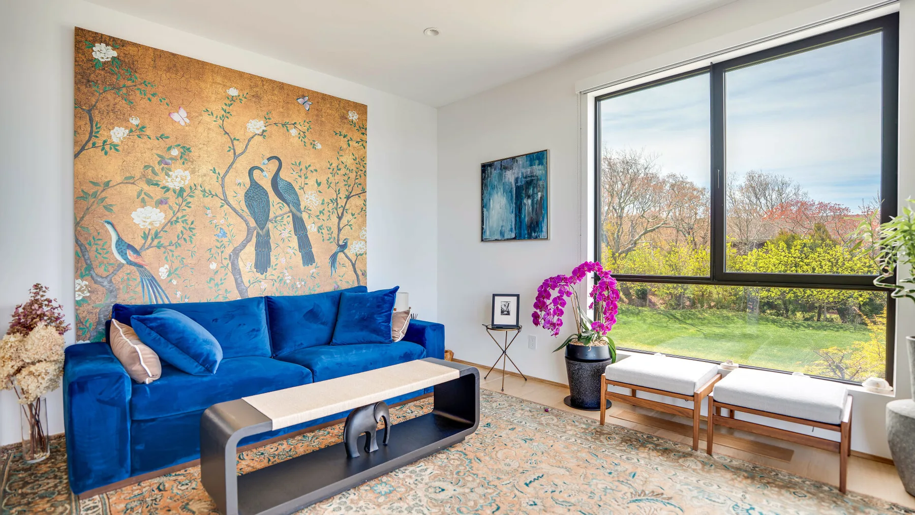 A living room with blue seating, wall art, and a large window overlooking greenery.