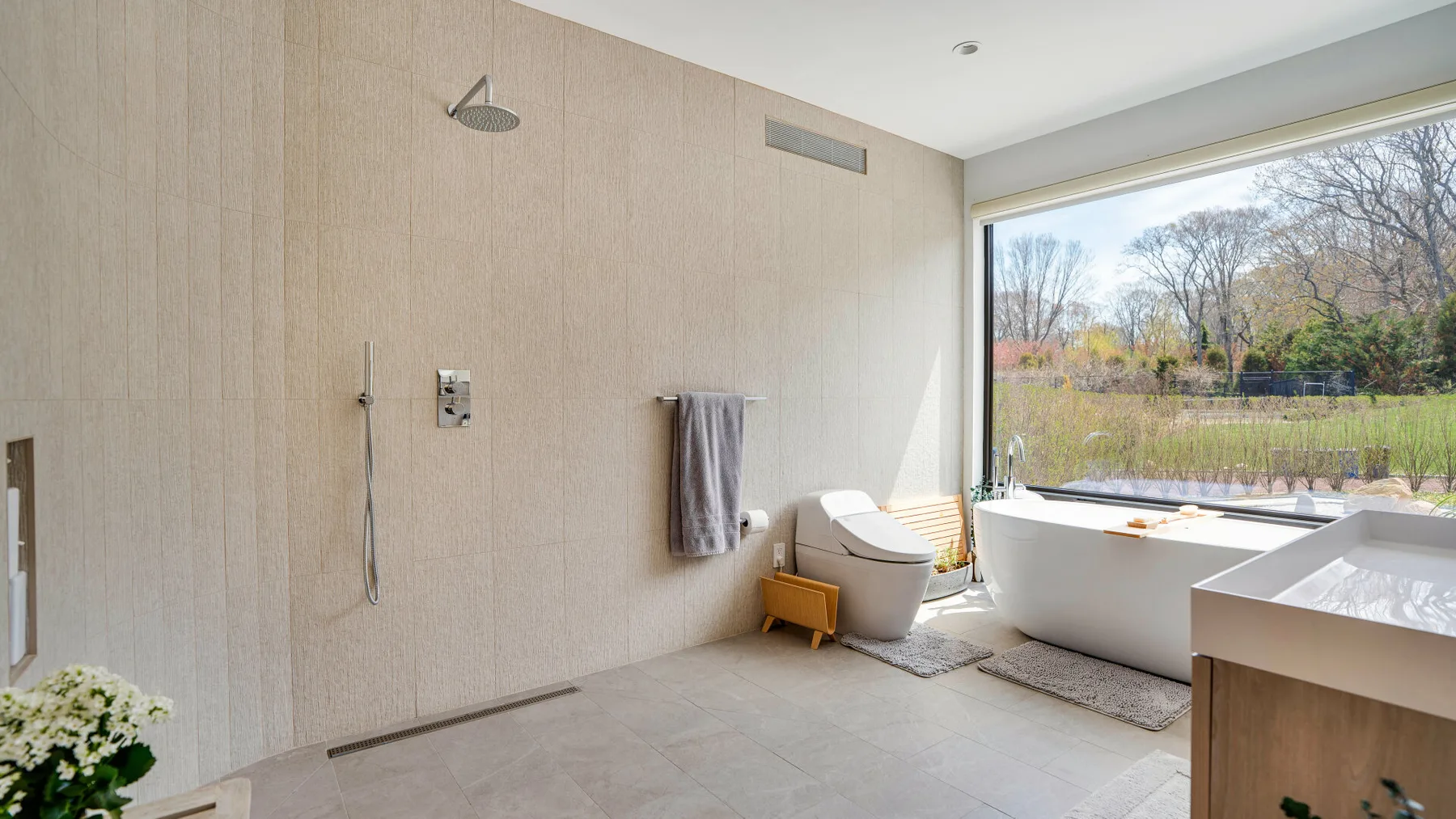 A bright bathroom has a bathtub beside a large window overlooking trees.
