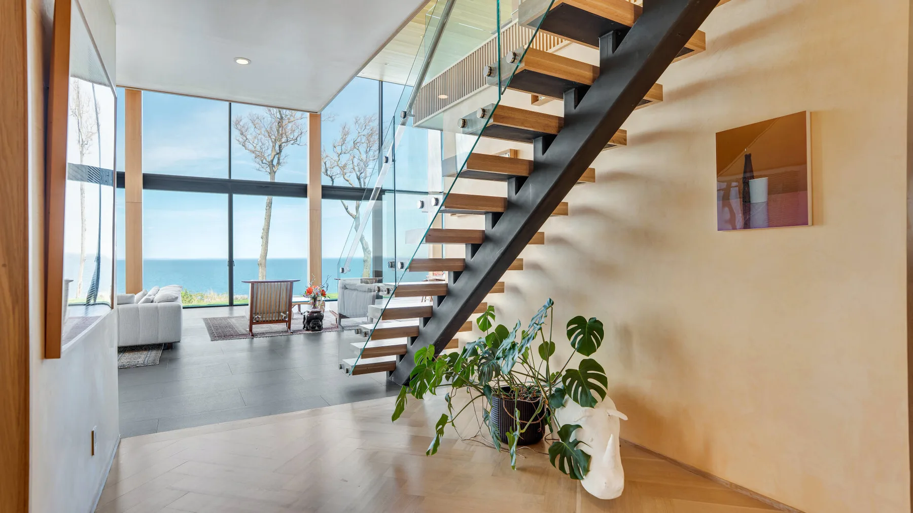 A bright living room with large windows, seating, and an open staircase.