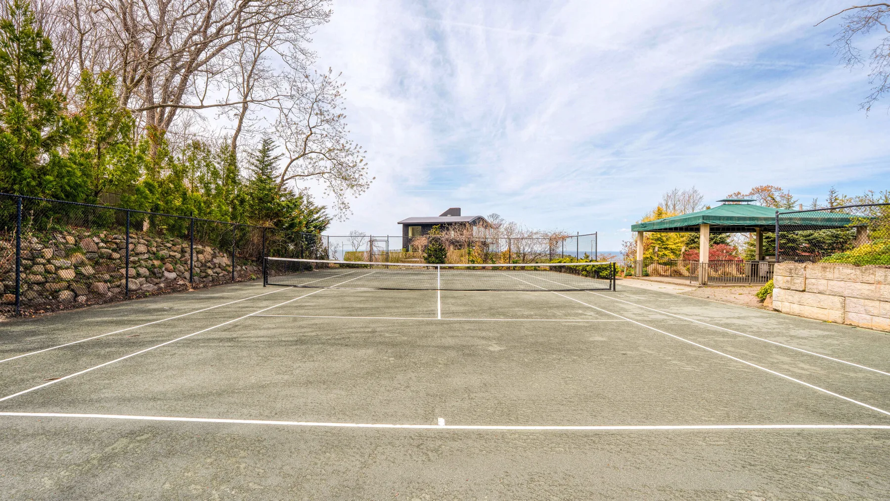 An outdoor tennis court is surrounded by trees and fencing.