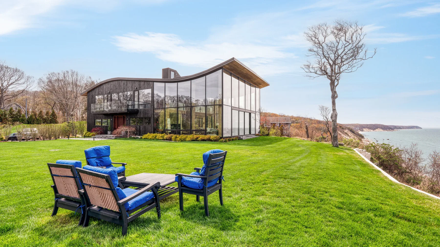 A modern glass house overlooks a broad lawn beside the water.