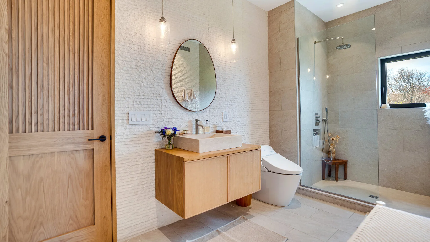 A modern bathroom with a wood vanity, toilet, and glass shower.
