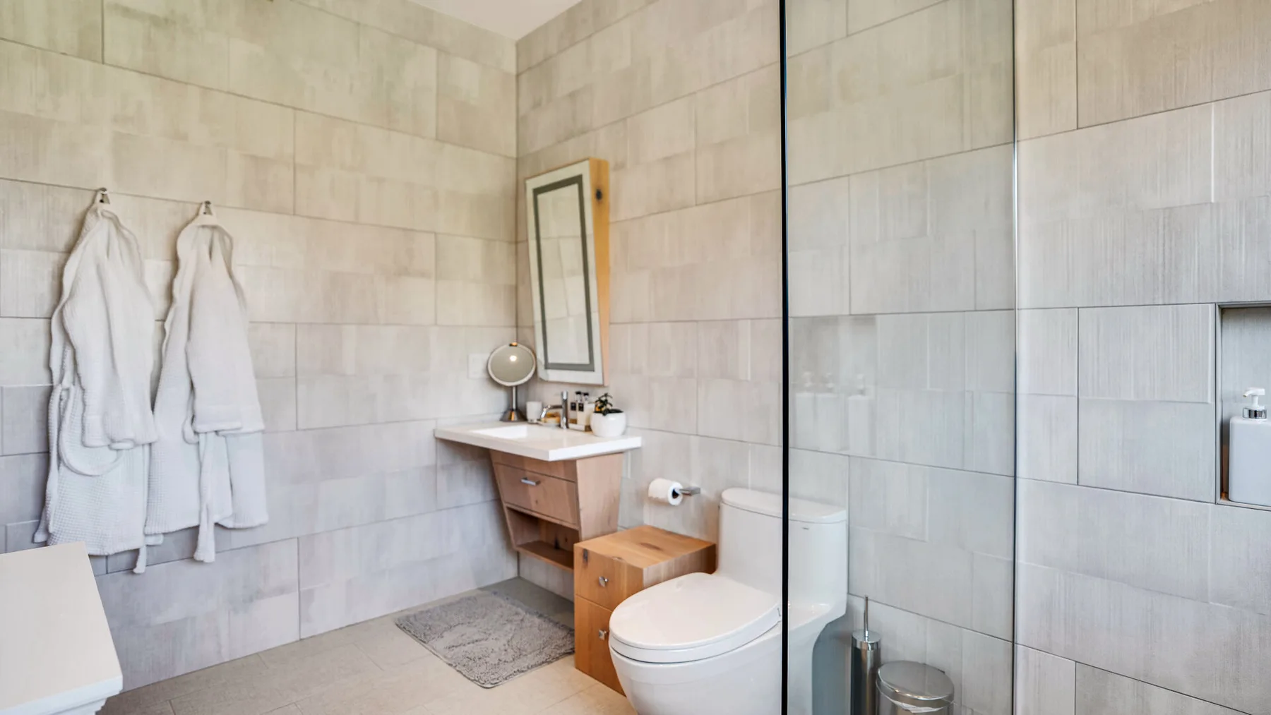 A tiled bathroom with a vanity, toilet, and glass shower partition.