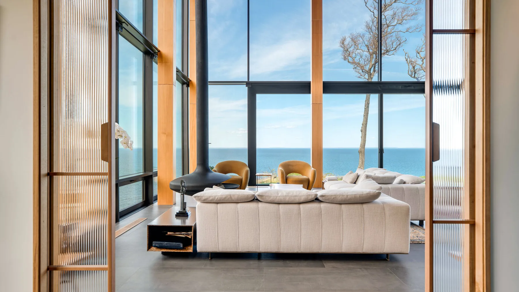 A bright living room with a sofa facing large windows and a view of the sea.
