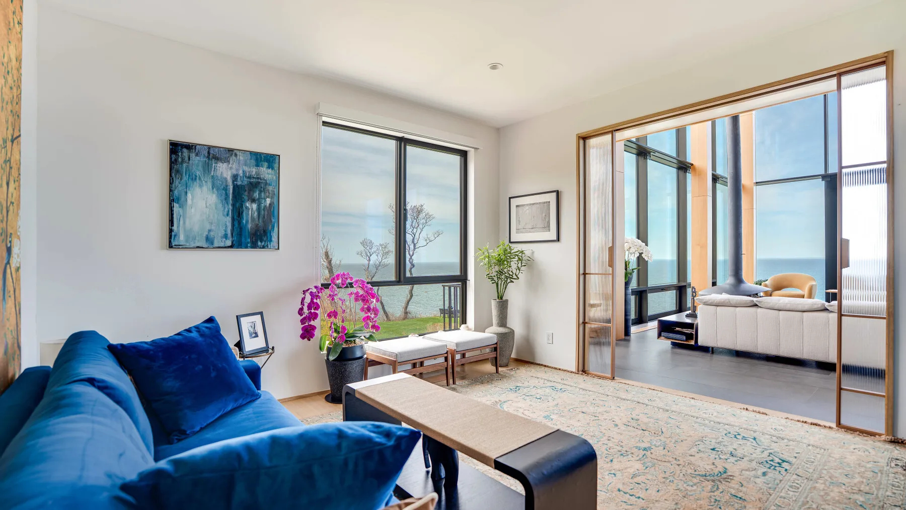 A bright living room with blue seating, a coffee table, and large windows.
