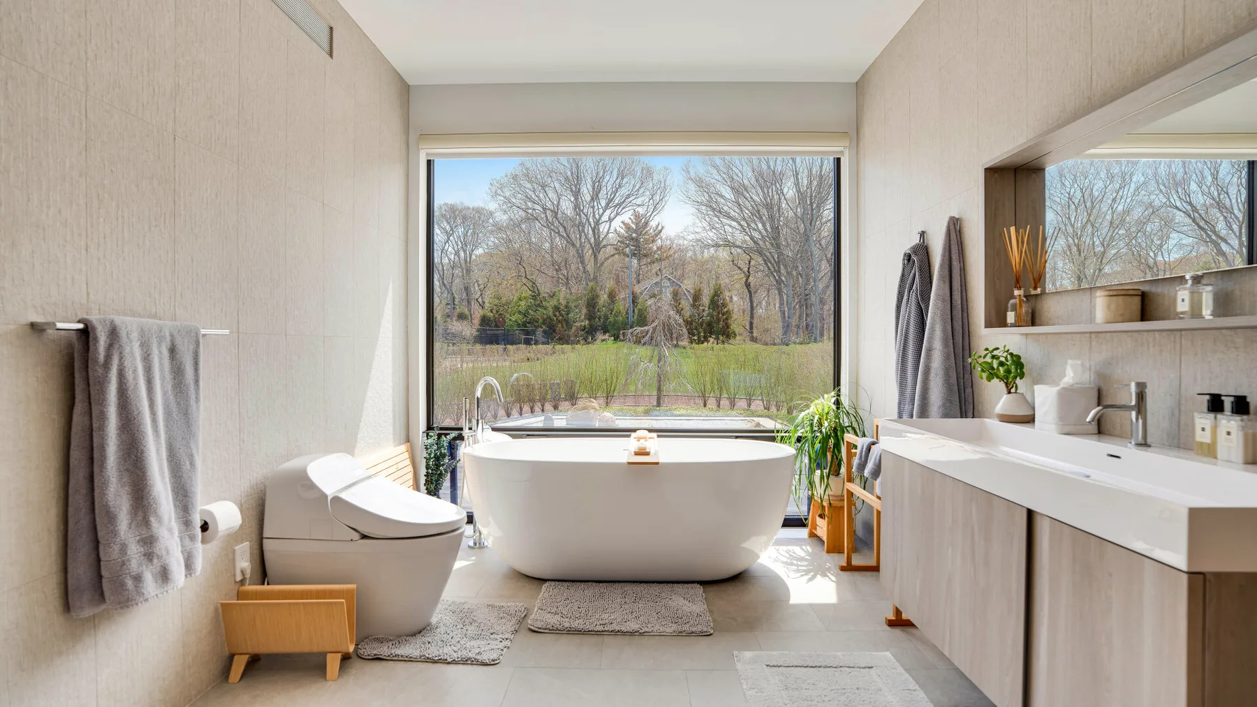 A bright bathroom with a freestanding bathtub beside a large window.