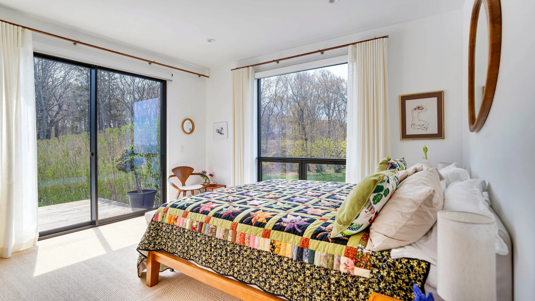 A bedroom with a colorful quilted bed beside large windows overlooking trees.